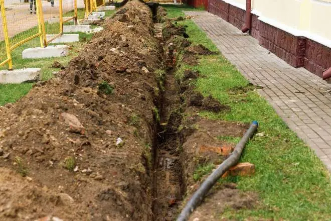 A long and deep trench dug up in a yard to lay in a drainage pipe for a trench drain