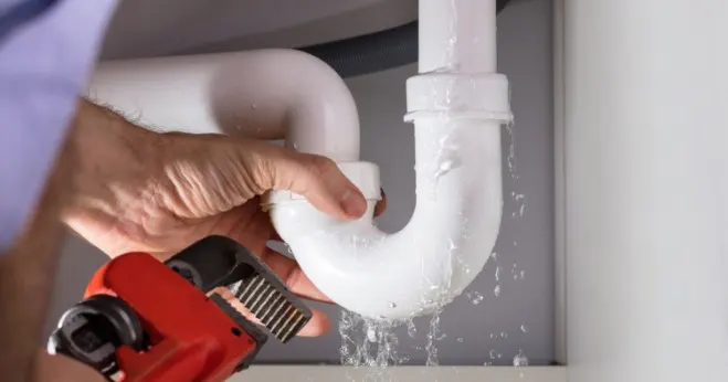 Plumber fixing leaky pipes under sink